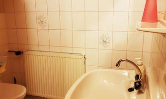 A small bathroom with a sink, a toilet, and a heater. The walls are tiled, and a wooden ceiling adds warmth.