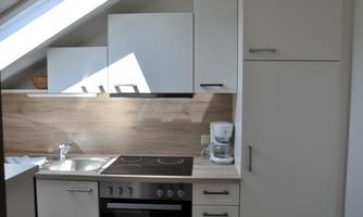 A modern kitchen with bright furniture and a wooden countertop. There is a stove, a sink, and a coffee machine.