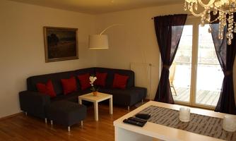 A modern living room with a gray sofa and red cushions. Large windows let in plenty of light, and the decor is stylish and inviting.