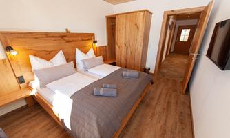 A modern bedroom with two beds and wooden paneling. The room is bright and cozy, with large windows and warm colors.