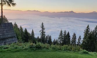 A beautiful view above the clouds with mountains in the background. The landscape is surrounded by trees and green grass.
