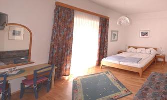 A bright room with a large bed and a cozy sofa. Colorful curtains hang at the window, and there is a table with chairs.