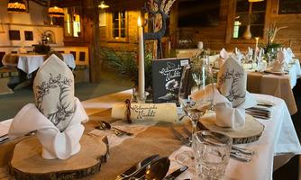 Ein elegant eingedeckter Tisch in einem rustikalen Restaurant. Die Dekoration umfasst geschmackvoll gefaltete Servietten, Holzuntersetzer und Kerzen.