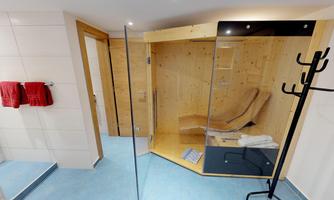 A modern sauna area with wooden paneling and glass walls. Towels hang close to the sauna and a relaxed atmosphere is present.