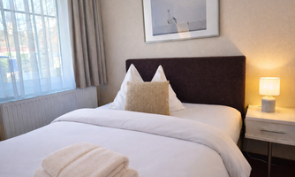 A cozy bedroom with a double bed and a modern lamp. A framed picture hangs on the wall, and there is a towel on the bed.
