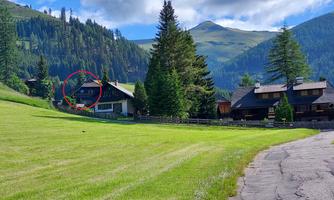 A picturesque landscape with green meadows and high mountains in the background. In the foreground, several houses and trees can be seen.