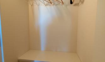 A small wardrobe with a shelf and a few hangers. The floor is made of wood and the walls are kept neutral.