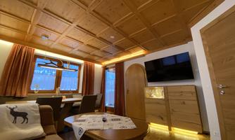 A cozy room with wooden walls and large windows. The room is warmly lit and features a modern television and an inviting seating area.
