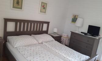 A cozy bedroom with a double bed and comfortable pillows. Next to the bed is a nightstand and a TV on a cabinet.