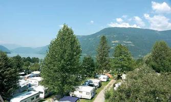 A tranquil campsite landscape with motorhomes amidst trees. In the background, mountains and a clear blue sky can be seen.