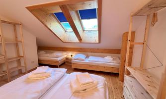 A bright room with skylights and two beds. There are simple wooden furniture and fresh bed linen.