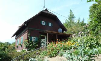 A charming red house surrounded by a blooming garden. The facade has green shutters and an inviting entrance.