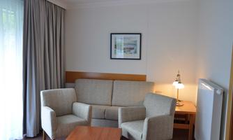 A cozy living room with a bright sofa and two armchairs. A small table and a lamp complete the decor.