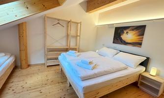 A cozy bedroom with two beds and a wooden shelf. A picture of a sunset hangs on the wall.