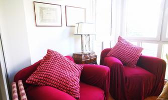Cozy red armchairs with checkered pillows are located in a bright room. A table with a lamp completes the decor.