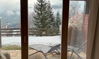 A conservatory with a view of snow-covered mountains. In the foreground, there are sun loungers on a terrace.