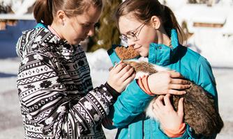 Two girls are standing outside holding cats. They look happy and are dressed in warm winter jackets.