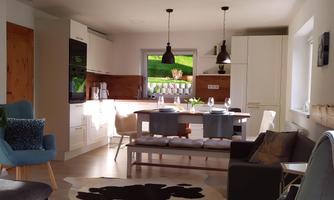 A modern kitchen with a dining area and plenty of natural light. The decor is bright and inviting, with a cozy sofa and stylish furniture.