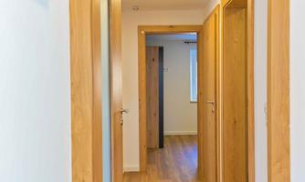 A bright hallway with wooden flooring and several doors. Coat hooks hang on the wall, and the space feels modern and inviting.