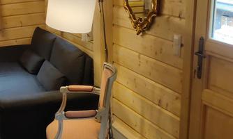A cozy living space with wooden-paneled walls. A black sofa and an elegant chair stand next to a lamp and a large mirror.