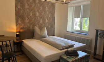 A cozy room with a bed and decorative wall patterns. The window lets in a lot of daylight.