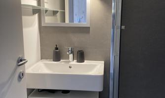 A modern bathroom with a sink, a mirror, and a shower. It has bright walls and a tidy, minimalist design.
