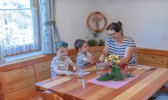 A mother is sitting at the table with two children. Together, they are preparing the meal in a cozy environment.