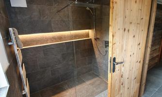 A modern tiled shower with glass walls and wooden details. The lighting creates a pleasant atmosphere.