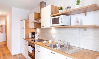 A modern kitchen with wooden shelves and white cabinets. It is well-equipped with a sink, stove, and microwave.