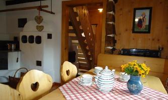 A cozy dining area with a wooden chair and table, set with a checked tablecloth. In the background, there is a staircase and rural style decor.