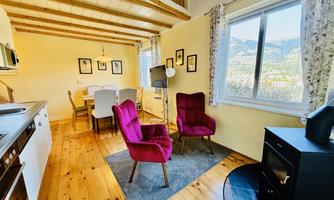 A cozy living space with modern furniture, including two pink armchairs. Large windows offer a view of the countryside.