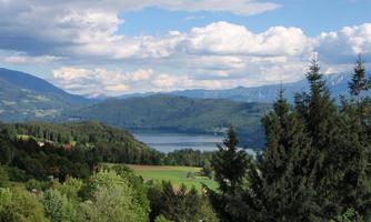 A picturesque landscape with mountains, a green valley, and a lake. The sky is partly cloudy and nature is lush and inviting.