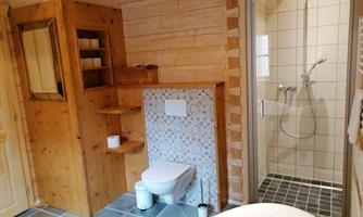 A rustic bathroom with wooden paneling and modern elements. The shower is clearly separated, and the bathtub fits harmoniously into the space.