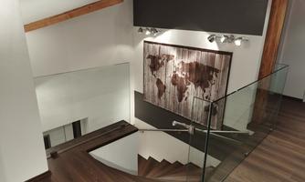 A modern staircase with wooden floor and glass railing. A world map in rustic design hangs on the wall.