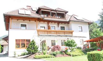 A beautiful, modern house with a balcony and large windows. The well-maintained garden is designed with green bushes and flowers.