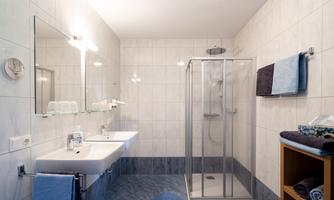 A modern bathroom with a shower and two sinks. Bright tiles and towels in various colors create a pleasant atmosphere.