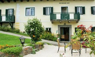 A cozy building with a balcony and green shutters. In the foreground are a garden and seating for relaxation.