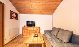 A cozy living room with a blue couch and a wooden table. An artwork hangs on the wall and a television is in the room.