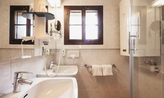 A modern bathroom with a glass shower and two sinks. Bright walls and large windows create a friendly atmosphere.