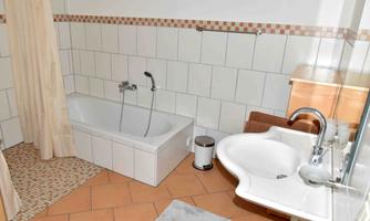 A simple bathroom with a bathtub and a sink. The walls are tiled and the floor is made of terracotta.
