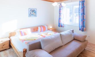 A bright bedroom with a double bed and a sofa. Large windows let in plenty of daylight.