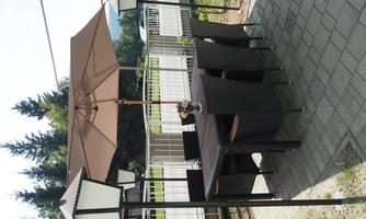 A cozy outdoor dining area with a table and chairs under a sunshade. Surrounded by trees and lantern-like lighting.