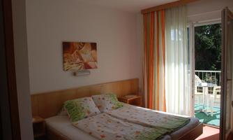 A cozy bedroom with a double bed and colorful curtains. The door leads to a balcony with a view.