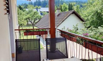 A cozy balcony with a table and chairs. In the background, there are trees and a cloudy sky.