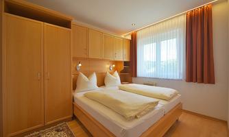 A cozy bedroom with two beds and light wood. Large windows provide plenty of daylight.