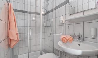 A modern bathroom with white tiles and a shower cabin. Towels in soft colors are ready.