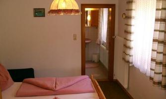 A simple bedroom with two beds and a warm lamp. In the background, a bathroom is visible.