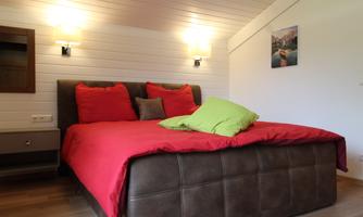 An inviting bedroom with a large bed and colorful cushions. The walls are bright and the lighting creates a cozy atmosphere.