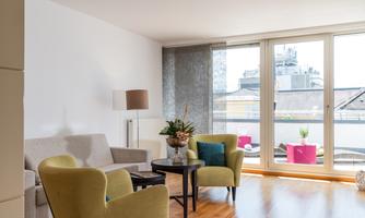 A modern living room with cozy furniture and large windows. The space is bright and offers a view of the city.