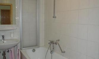 A modern bathroom with a bathtub and shower. The room is bright and equipped with white tiles.